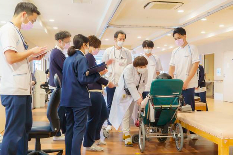 車いすの利用者を囲み、様々な職種のスタッフが話し合う様子