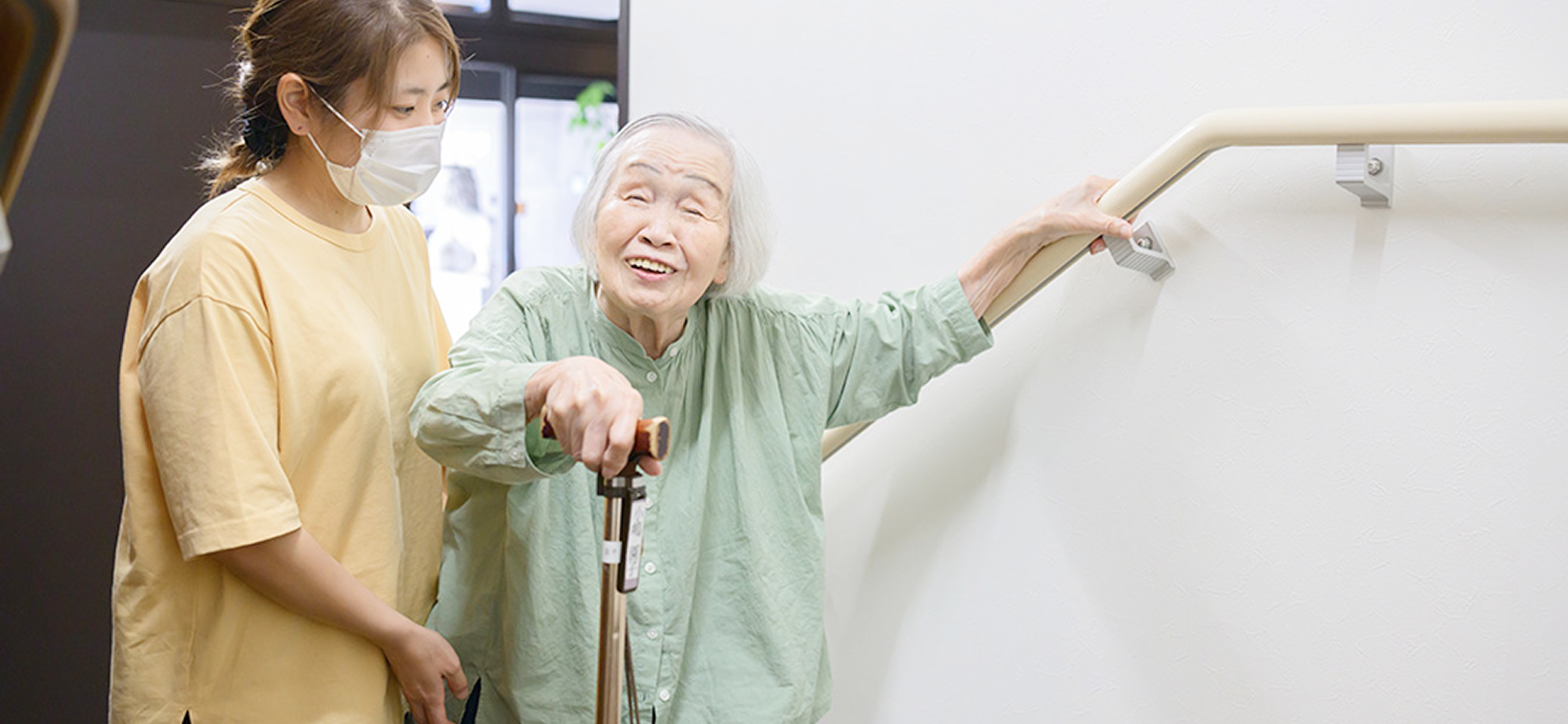 杖をつき手すりを使って階段を上る利用者に付き添うスタッフ
